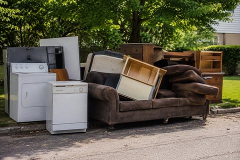 Pile of discarded household items including appliances, furniture, and wooden boxes on a driveway