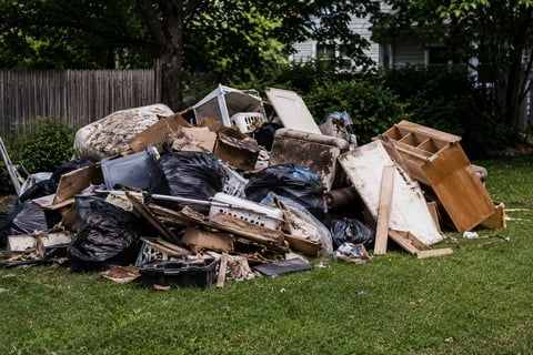 Large pile of discarded construction waste and debris on residential lawn including wood, metal, and cardboard materials