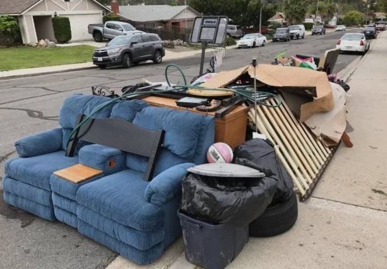 Blue upholstered armchair and discarded furniture piled on residential street curb for trash collection