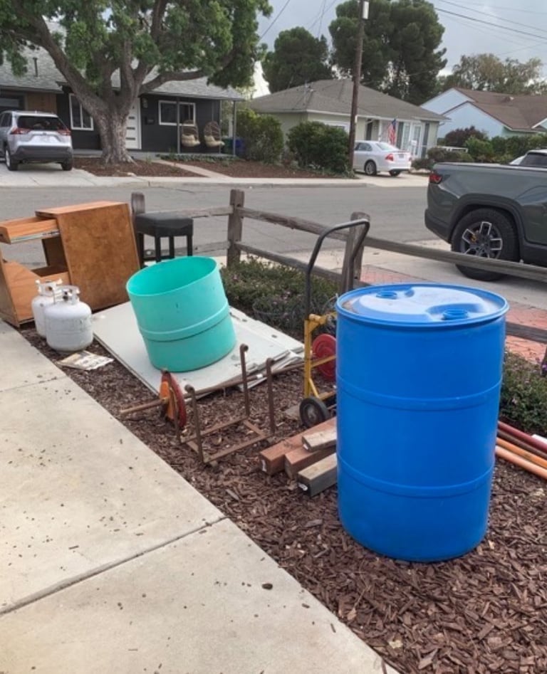 Blue and turquoise barrels with wood furniture and metal wagon displayed on residential sidewalk and yard
