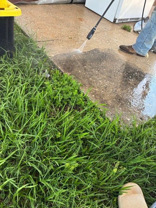 Person power washing a concrete driveway with an umbrella nearby to protect from water spray