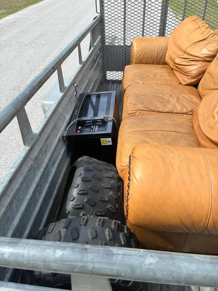 Truck bed containing tan/brown cushions, black tires, and equipment in metal utility trailer